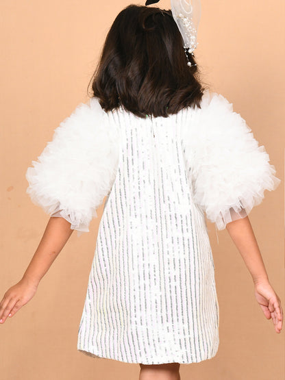A young girl wearing a glamorous white sequin dress with voluminous tulle frill sleeves, paired with silver heels. The knee-length dress shimmers under the light, making it perfect for special occasions like parties and weddings. Ideal for B2B wholesale and white-label manufacturing by Sundaram Fashions.